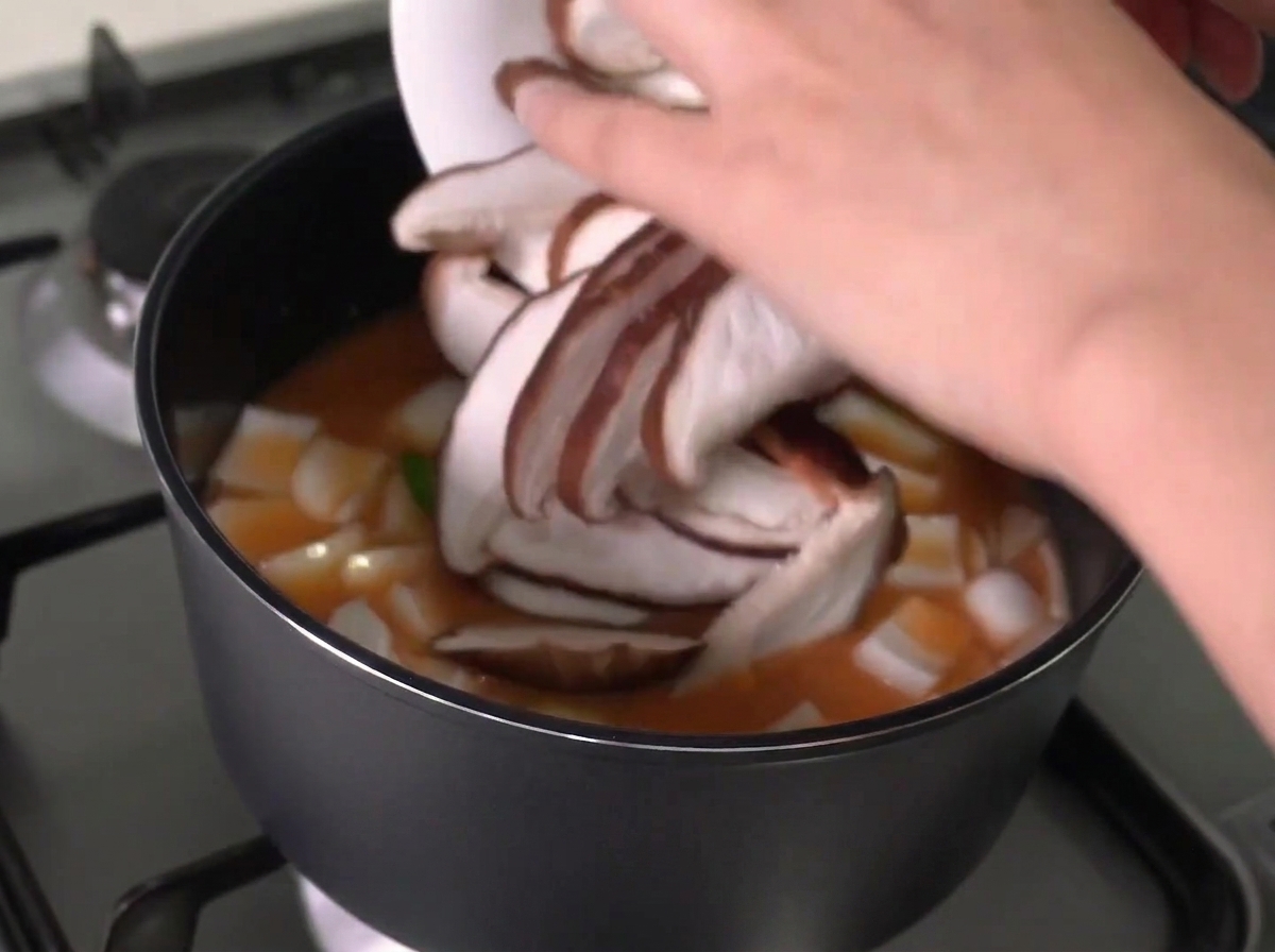 スライスしたシイタケを鍋に入れている様子。