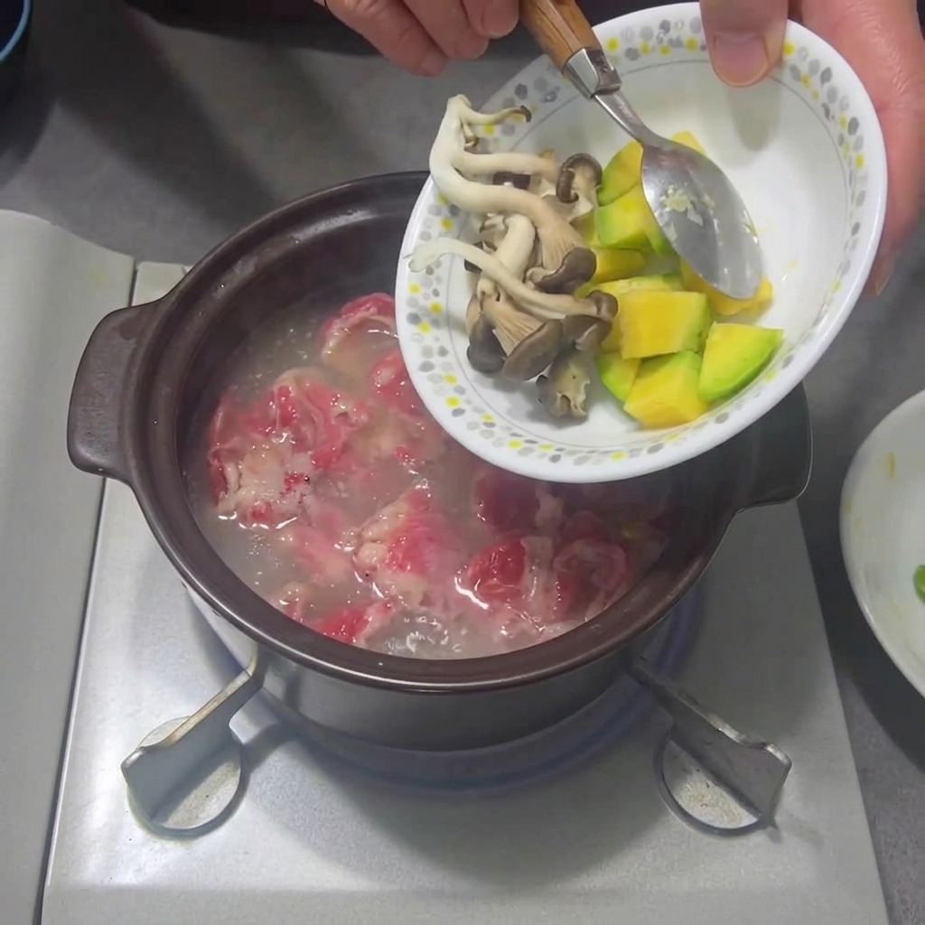 煮立っている鍋に、スライスしたキノコとズッキーニを加える様子。