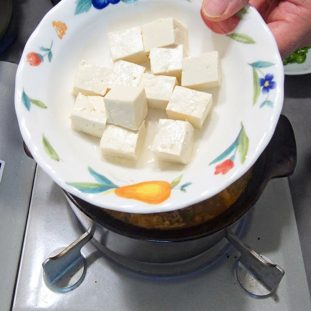 サイコロ状の白い豆腐を鍋にそっと入れる様子。