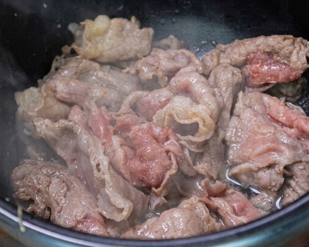 鍋の中で牛肉、にんにく、長ねぎが炒められている様子。