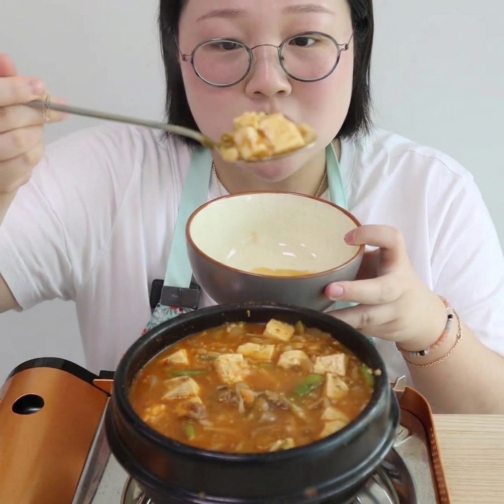煮立っているチゲに、角切り豆腐とえのきが加えられる様子。