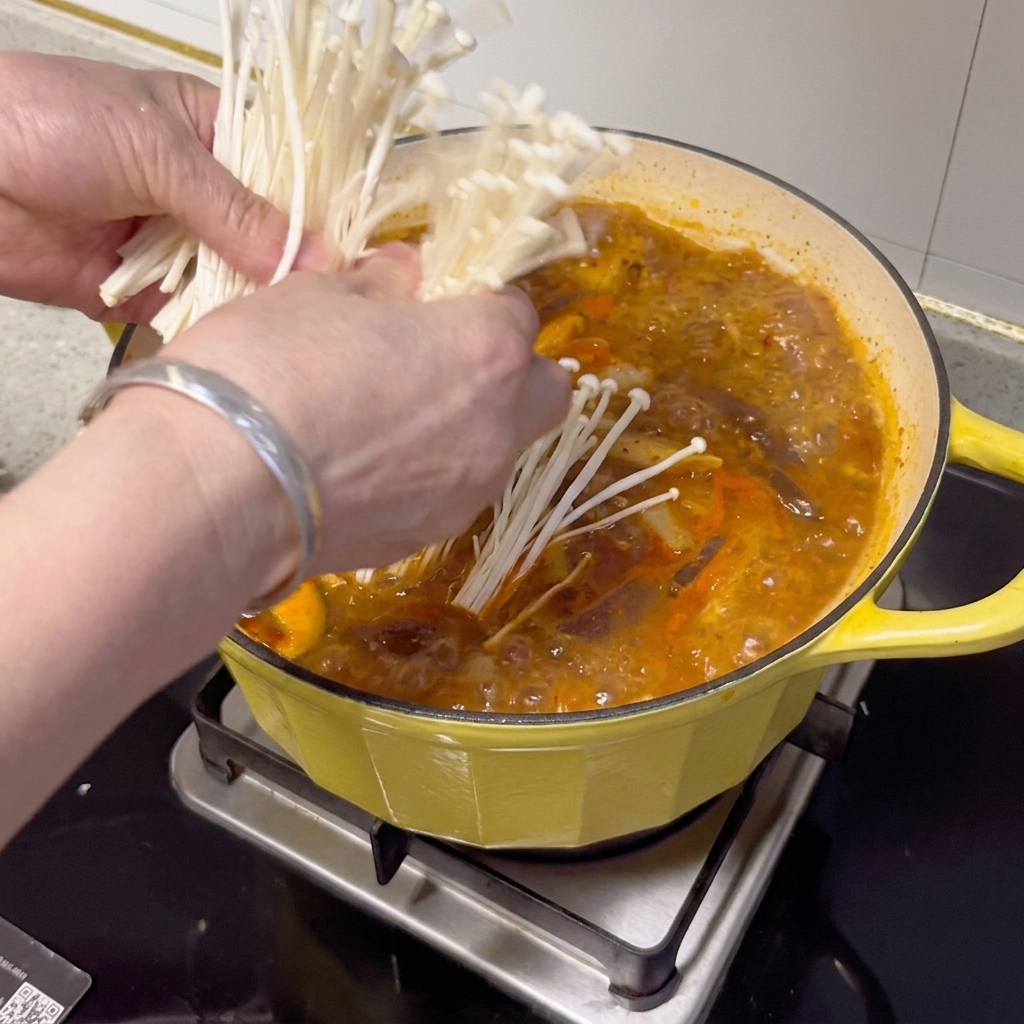 出来上がったチゲの上に、新鮮なえのき茸、長ねぎ、スライスした唐辛子が添えられている様子。