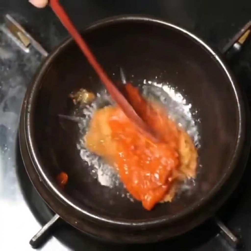 黒い鍋の中で、ドロッとした赤茶色の味噌を木べらで混ぜている様子。