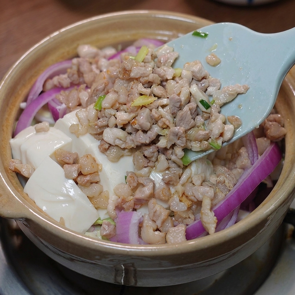 豆腐の上に炒めた肉とソースをかけている様子。
