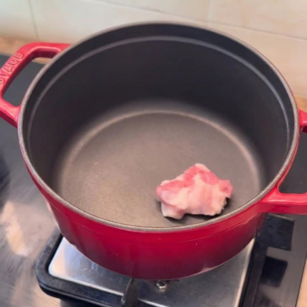 予熱した赤い鍋に豚バラ肉、くし切り玉ねぎ、みじん切りにんにくを入れたところ。