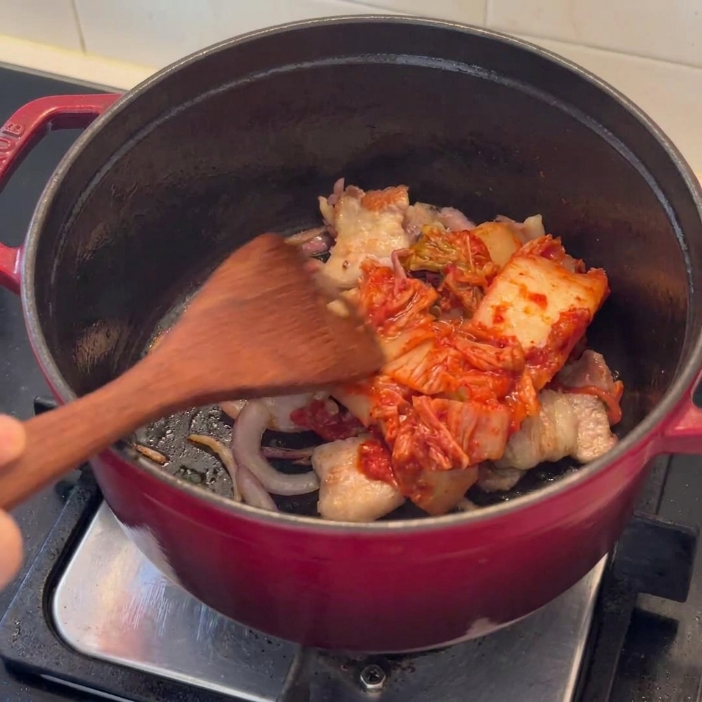 炒めた豚肉と一緒に鍋の中でキムチを炒め合わせる様子。