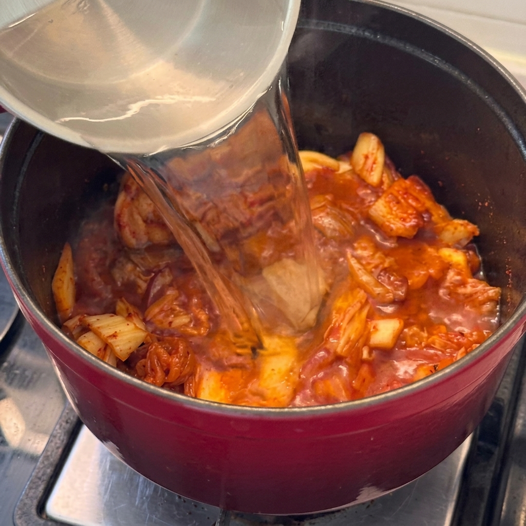 豚肉とキムチが入った鍋に水を注ぎ、スープを作る様子。