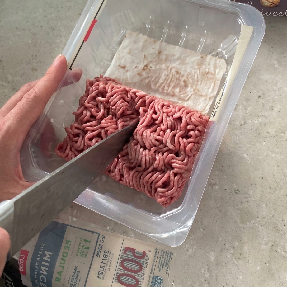 スーパーのパックに入った牛ひき肉を、大きな包丁で半分に切り分けている様子。