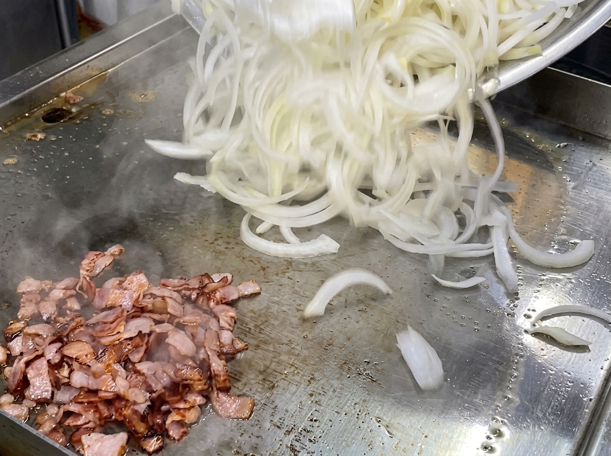 炒めたベーコンの横に、カットした生の白玉ねぎを山盛り投入している様子。