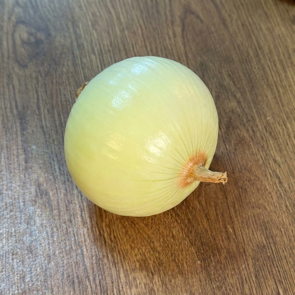 木のまな板の上に置かれた、皮をむいた丸ごとの玉ねぎ。