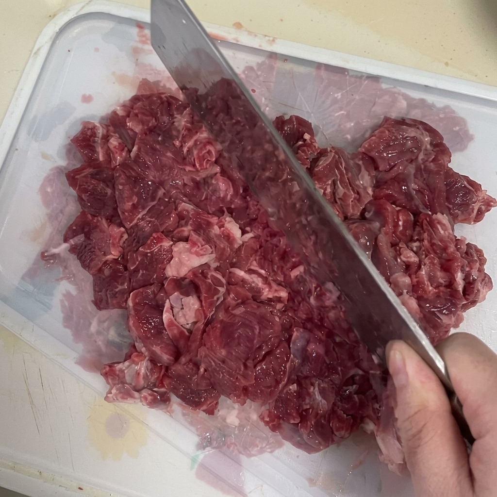 まな板の上で包丁を使って牛肉を細かくミンチにしている様子。