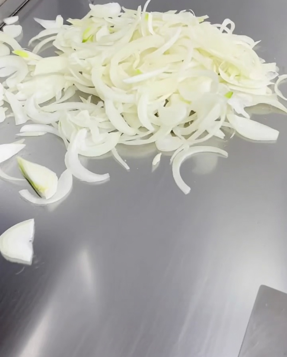 熱い鉄板の上で広げられた薄切りの白玉ねぎ。