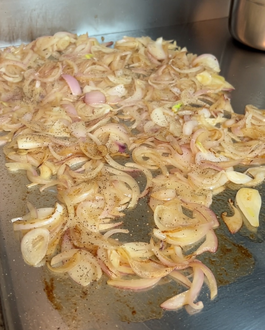 鉄板の上でキャラメリゼしている玉ねぎに、黒こしょうと鮮やかなスイートパプリカを振りかけている様子。