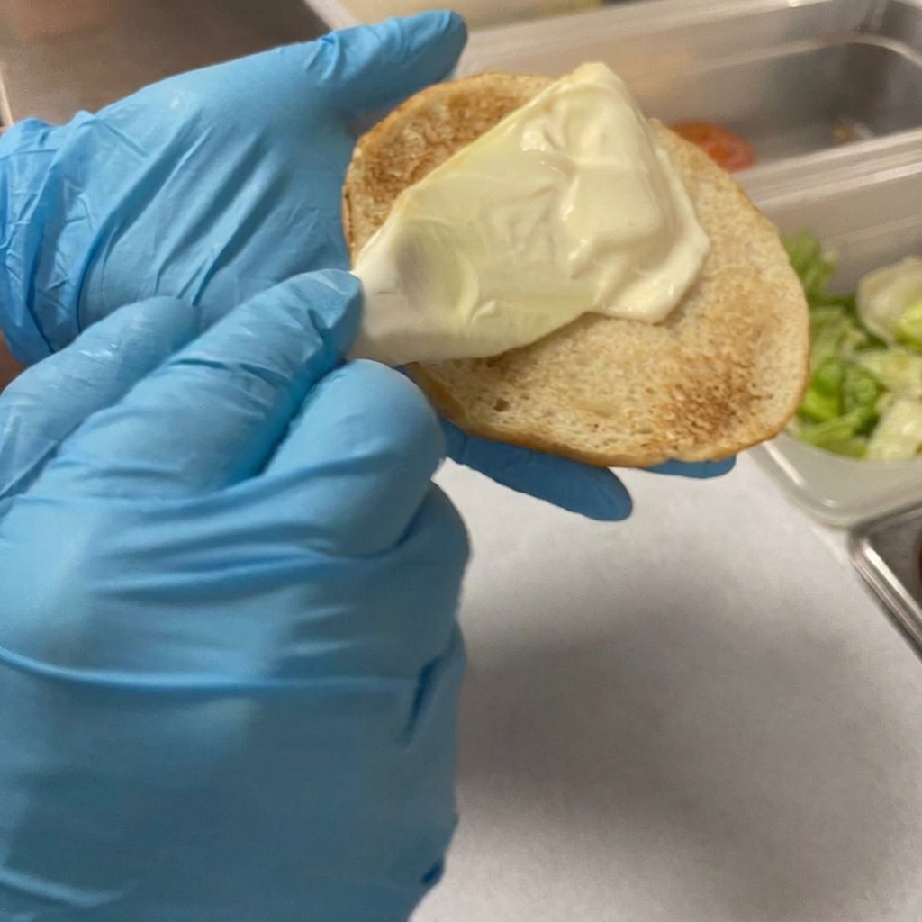 プラスチック製のスプレッダーで、トーストしたバンズにマヨネーズを塗っている様子。