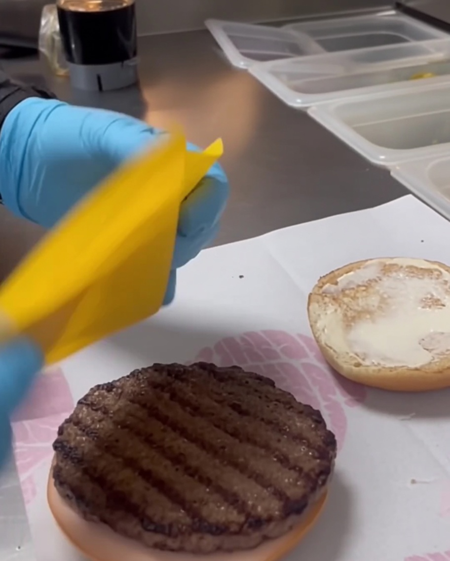 グリルしたビーフパティの上にスライスされたチェダーチーズが乗っている様子。