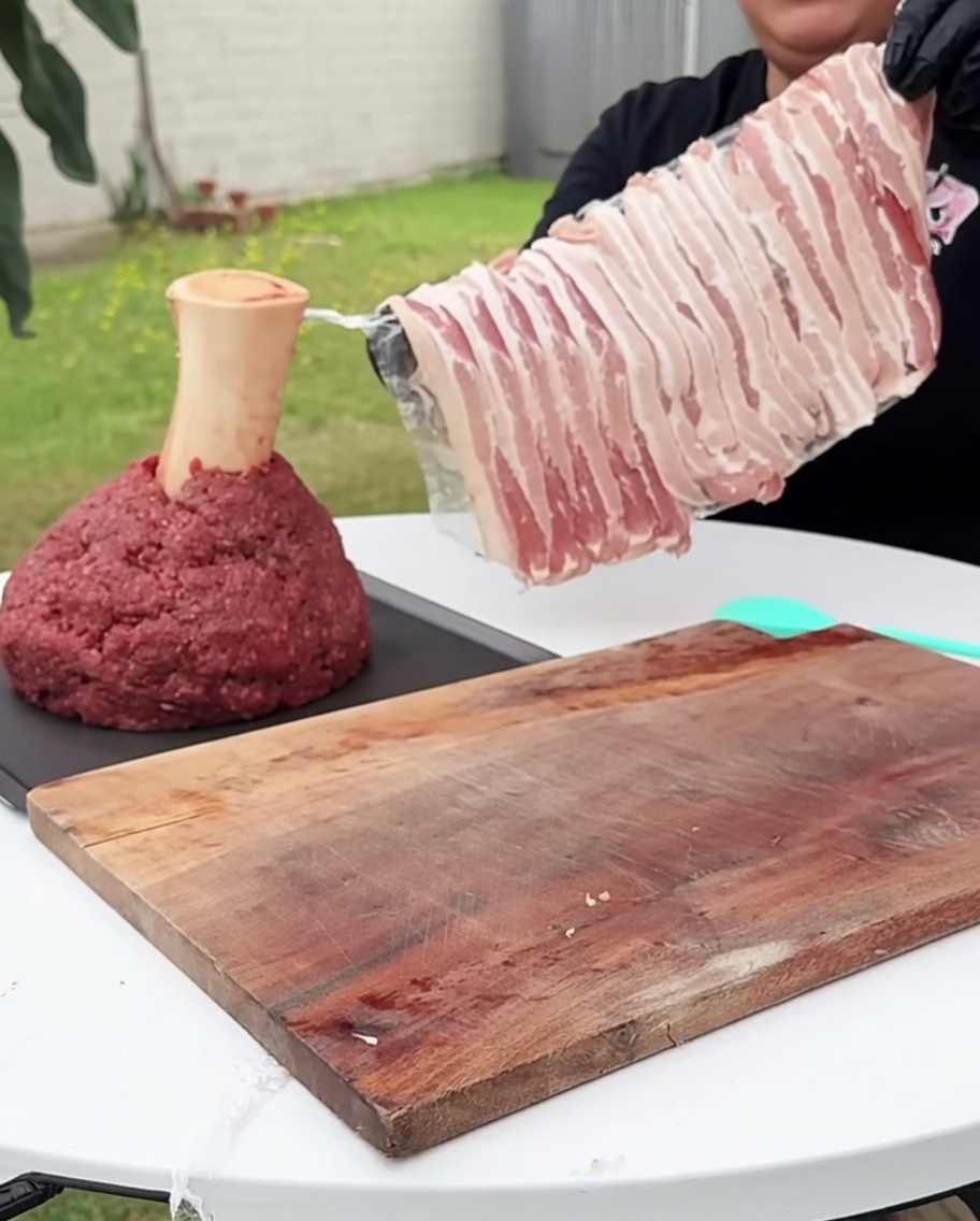 四角い牛挽肉の塊が、生のベーコンで丁寧に包まれている様子。