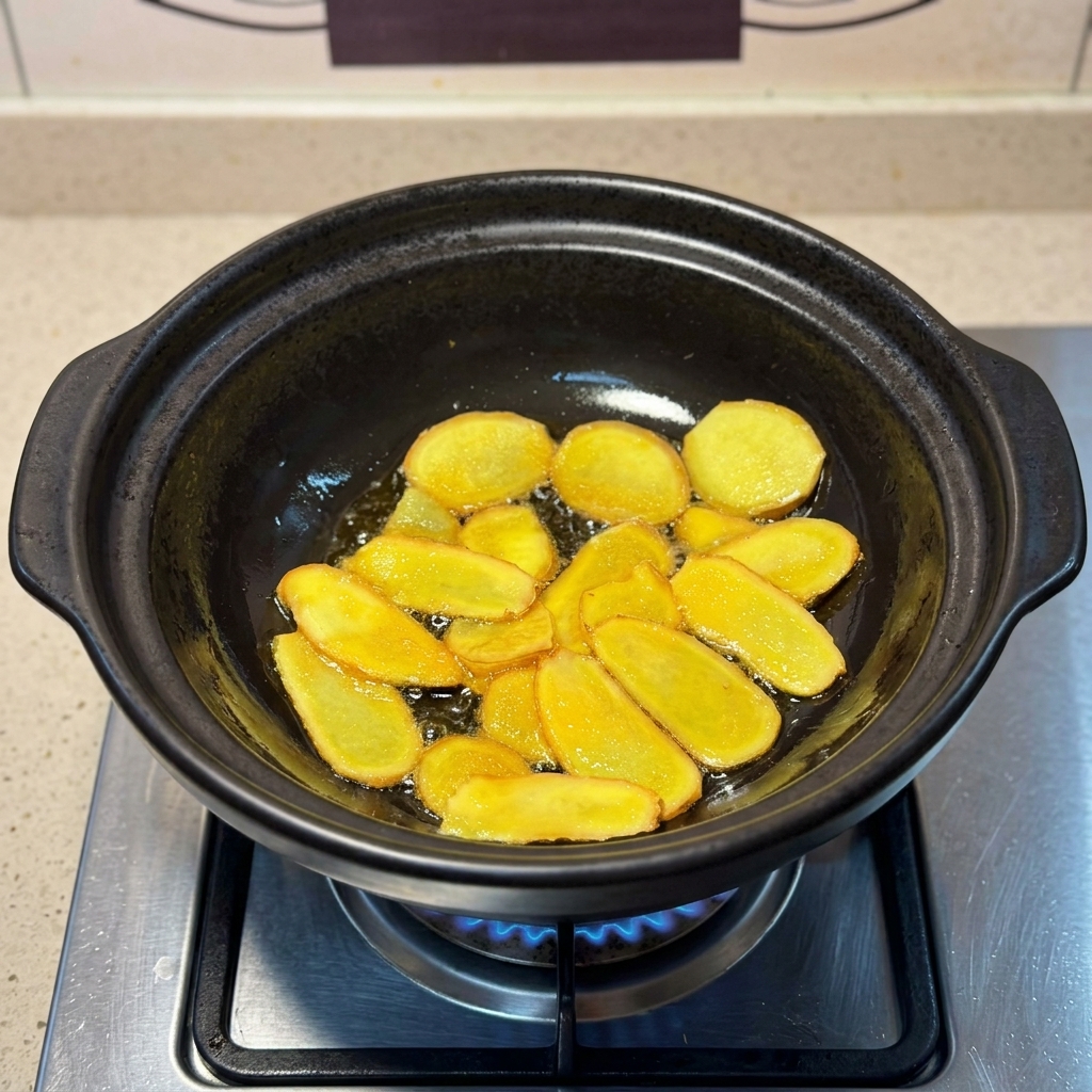 土鍋の中で、キラキラと光るごま油で揚げ焼きにされているきつね色の生姜スライス。
