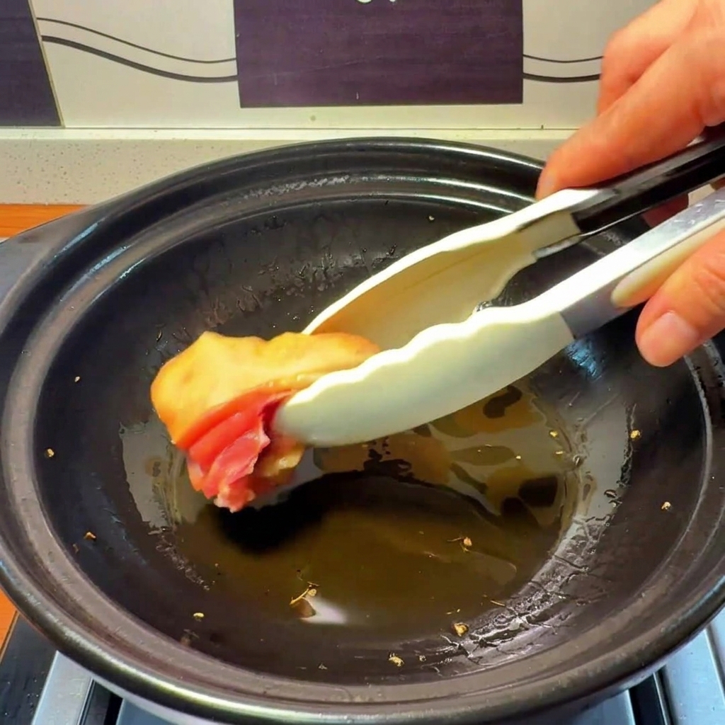 生姜の香りが移った熱い油の入った土鍋に、生の鶏肉を入れている様子。