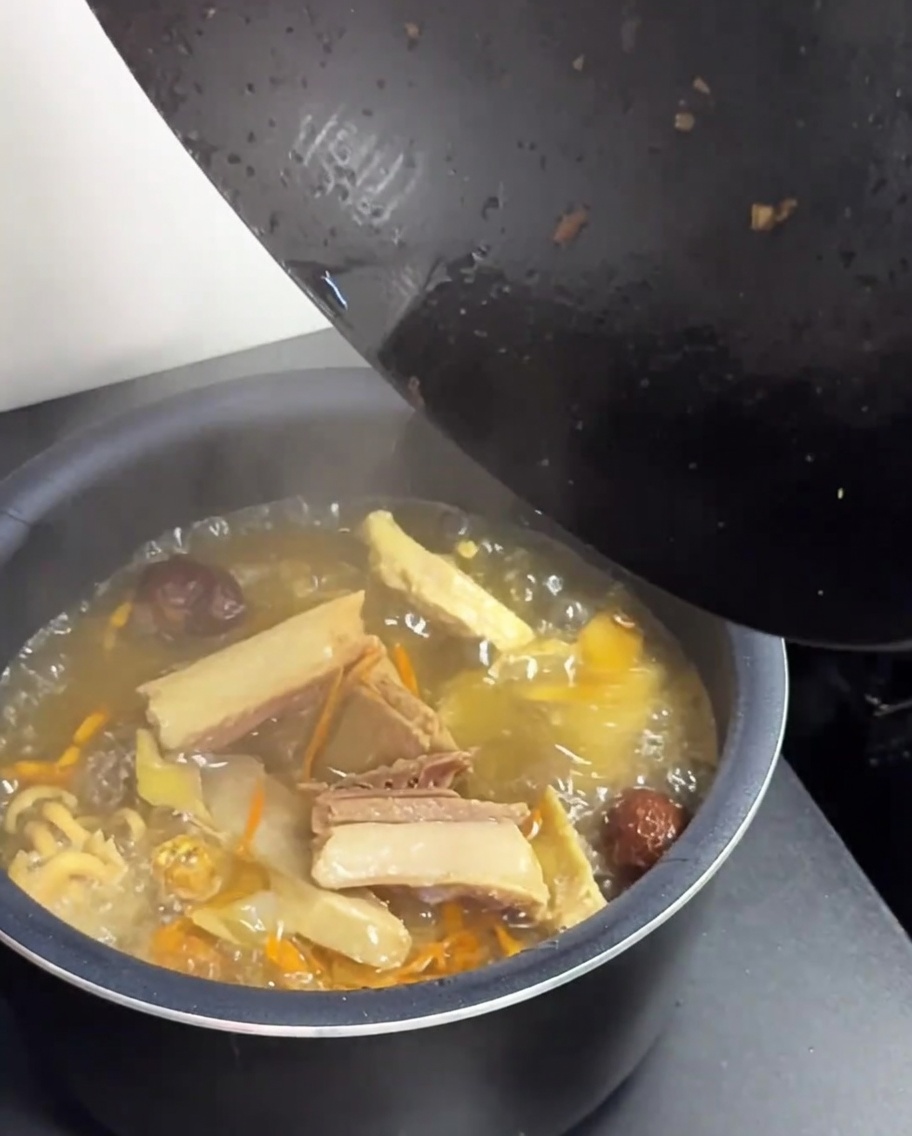 熱々の鶏肉ときのこのスープを黒い中華鍋から緑色の炊飯器の釜に移す様子。