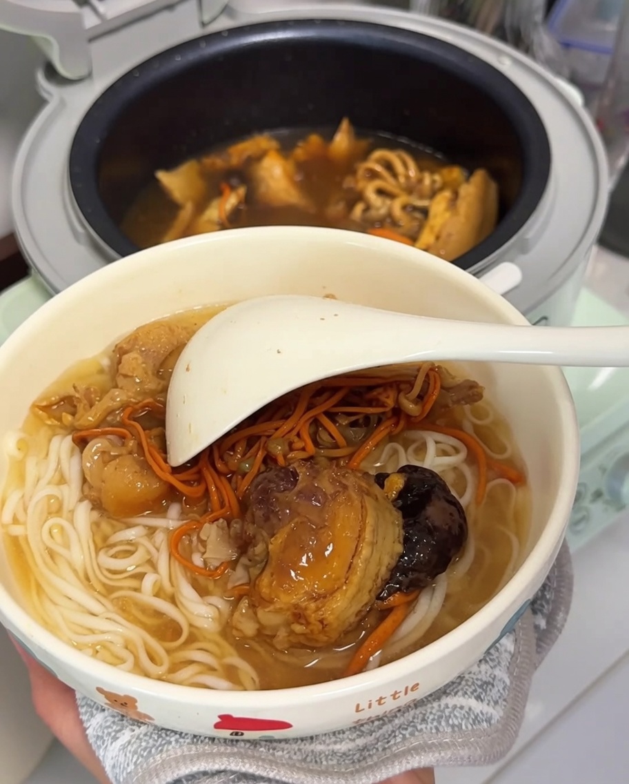 茹でた白い麺、鶏肉、乾燥きのこが入った器に、大きな白いおたまが添えられ、提供の準備が整った様子。