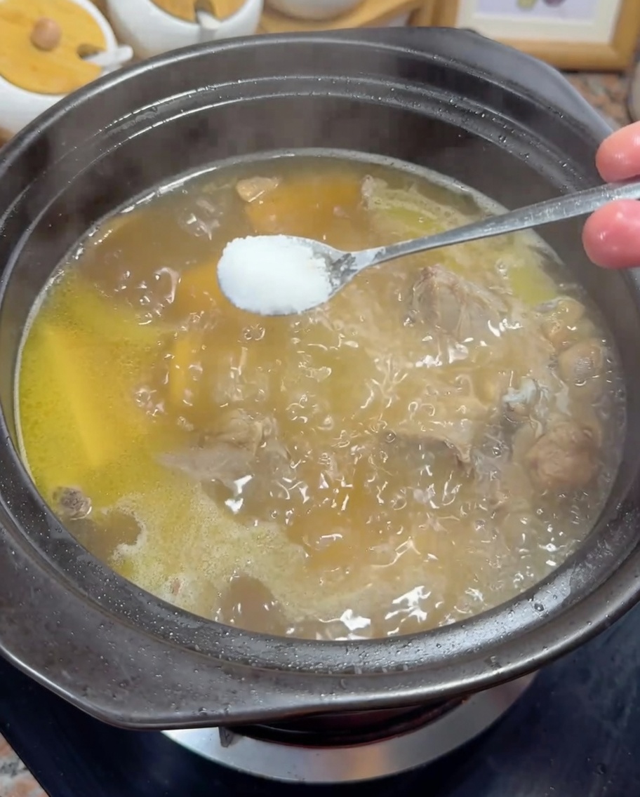 黄金色のスープに少量の塩を加えている様子。