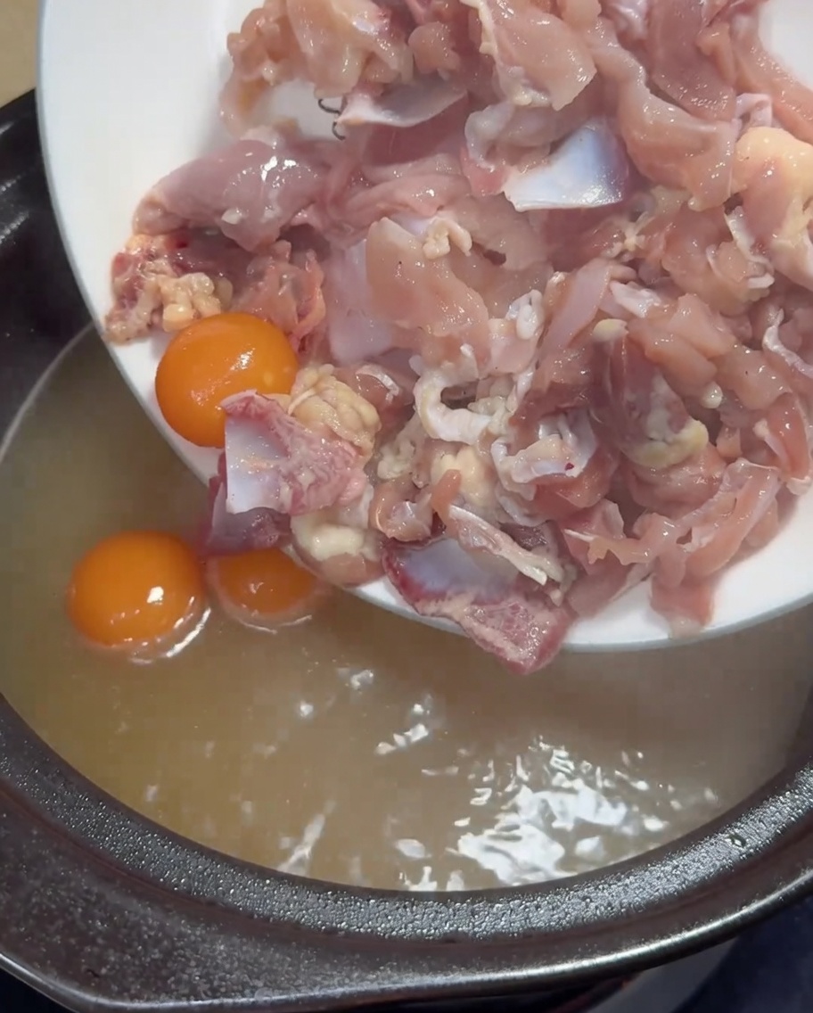 沸騰するスープに薄切り鶏肉と卵黄を入れている様子。