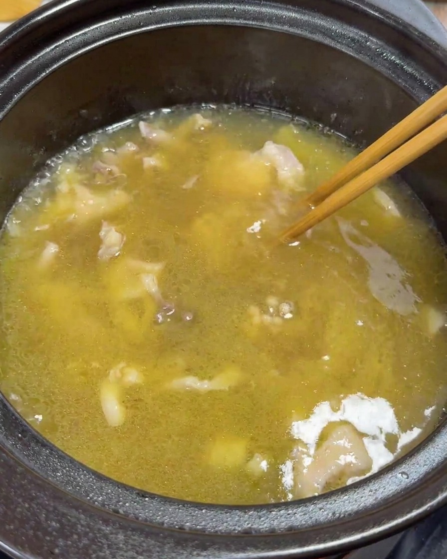 箸で鶏肉と卵黄をスープの中で優しく混ぜている様子。