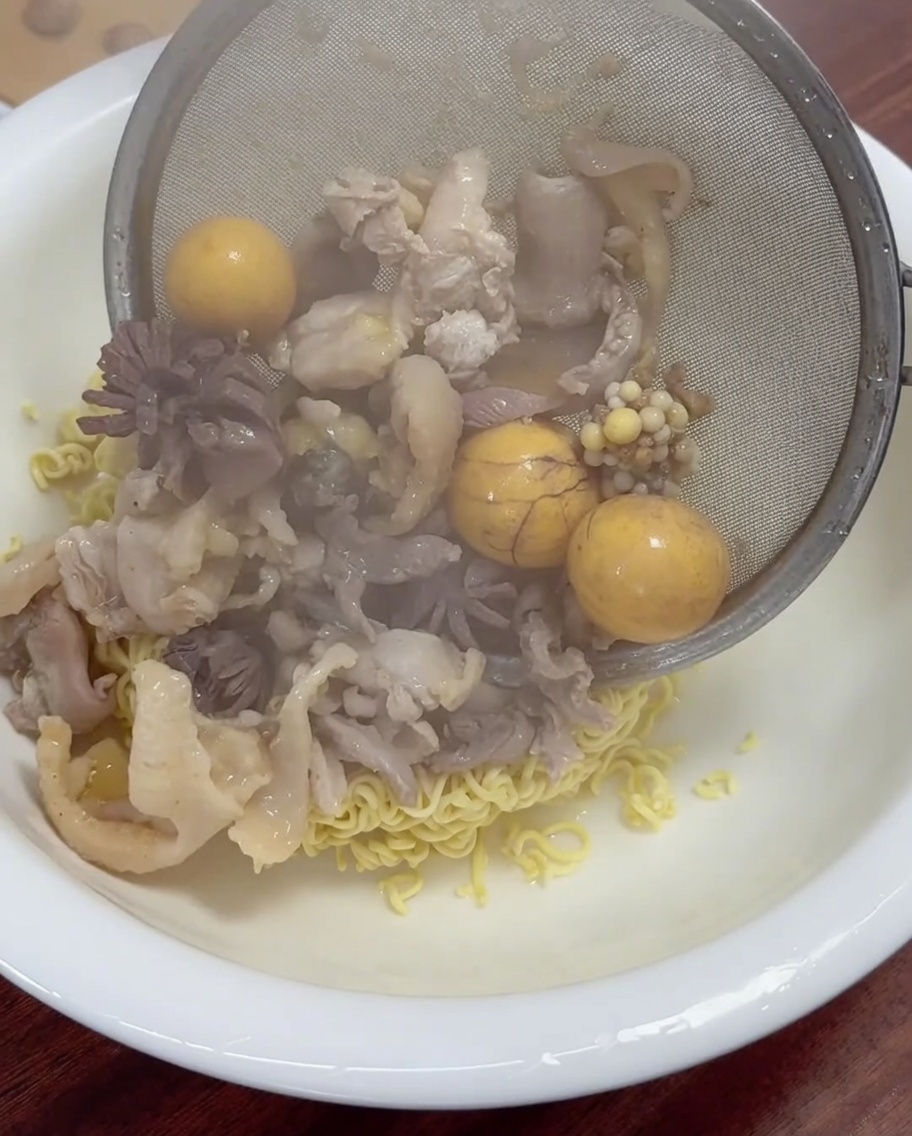 調理した鶏肉と卵黄を麺の上に盛り付けている様子。
