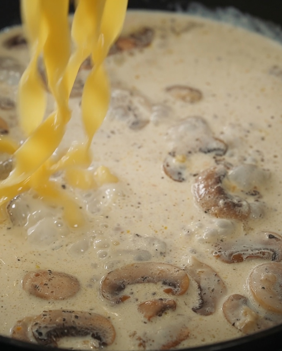 茹で上がったパスタをクリームソースに投入して混ぜている様子。