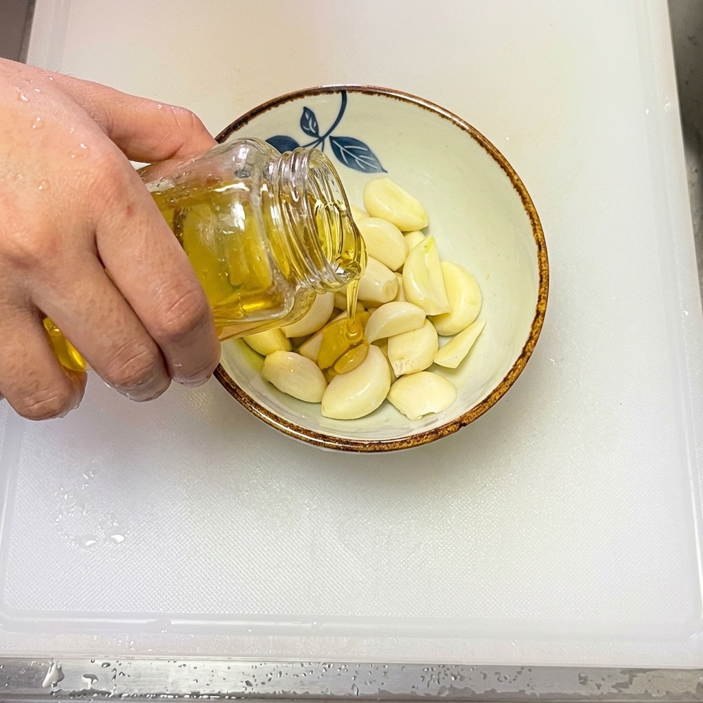 薄切りにしたにんにくが入ったボウルにオリーブオイルを注ぐ様子。