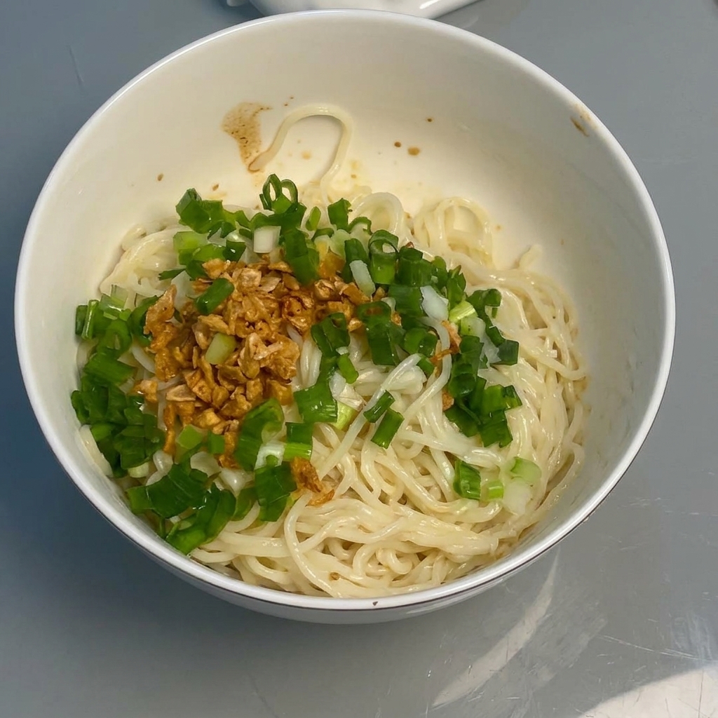 箸を使って麺をタレや薬味と混ぜ合わせる様子。