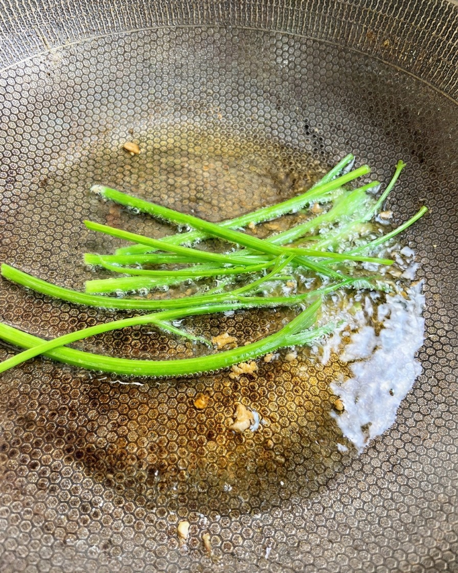 ニンニクのオイルに新鮮な緑色のパセリの茎が加えられている様子。