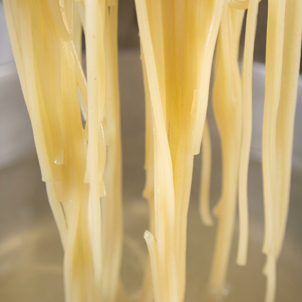 にんにくと赤唐辛子が入ったオイルのフライパンに、茹で上がったスパゲッティの麺を加えている様子。