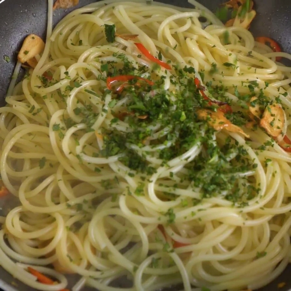 フライパンの中のスパゲッティとガーリックオイルソースの上に、刻んだ生パセリが散らされている様子。