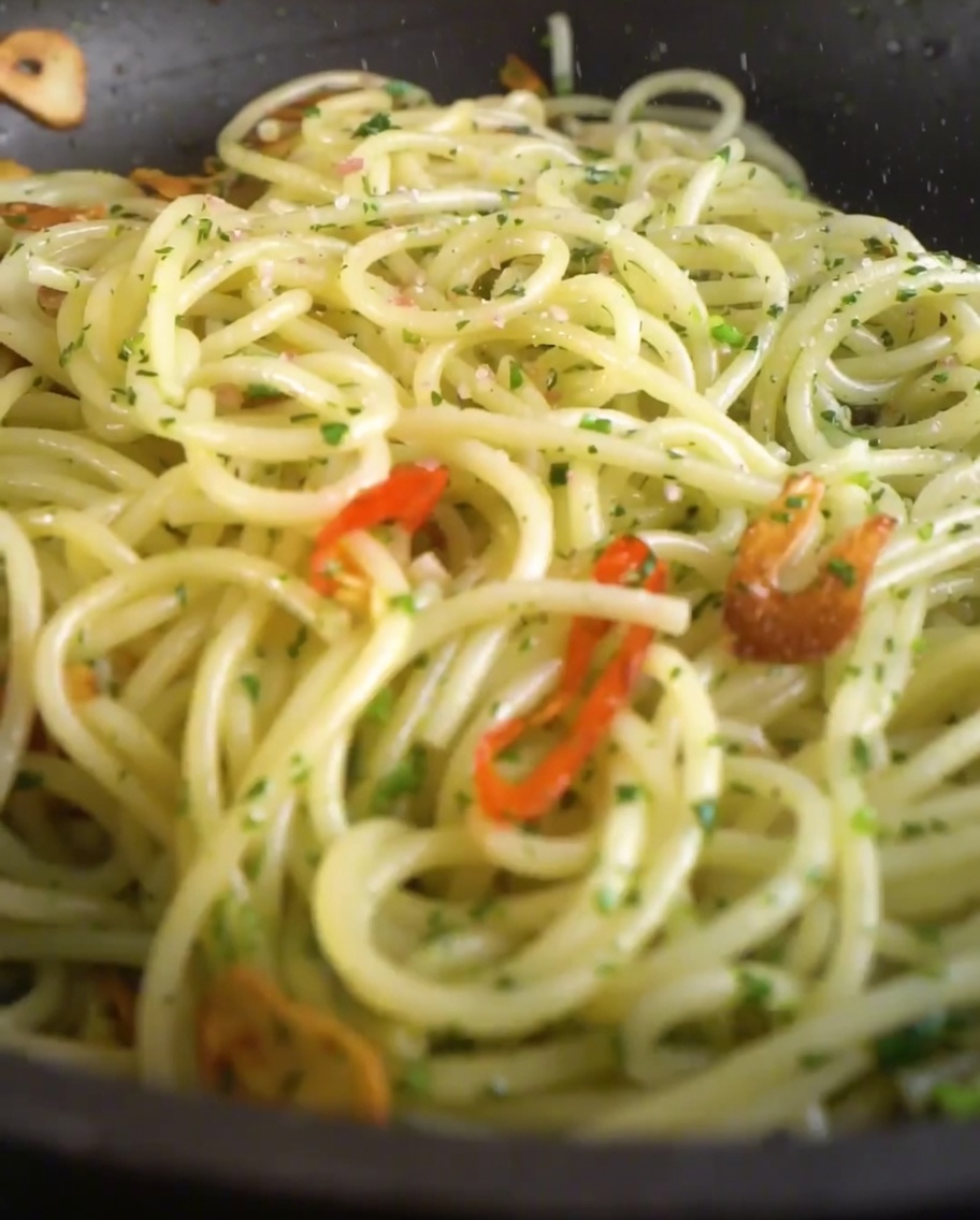 フライパンの中のパスタに、塩と挽きたての黒こしょうが振りかけられている様子。