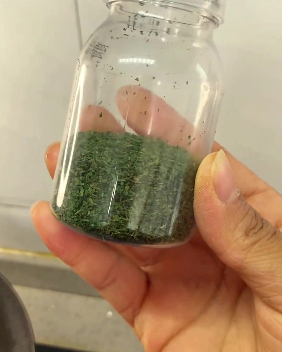 自家製の乾燥セロリパウダーが半分ほど入った、小さな透明なプラスチック瓶を持っている手。
