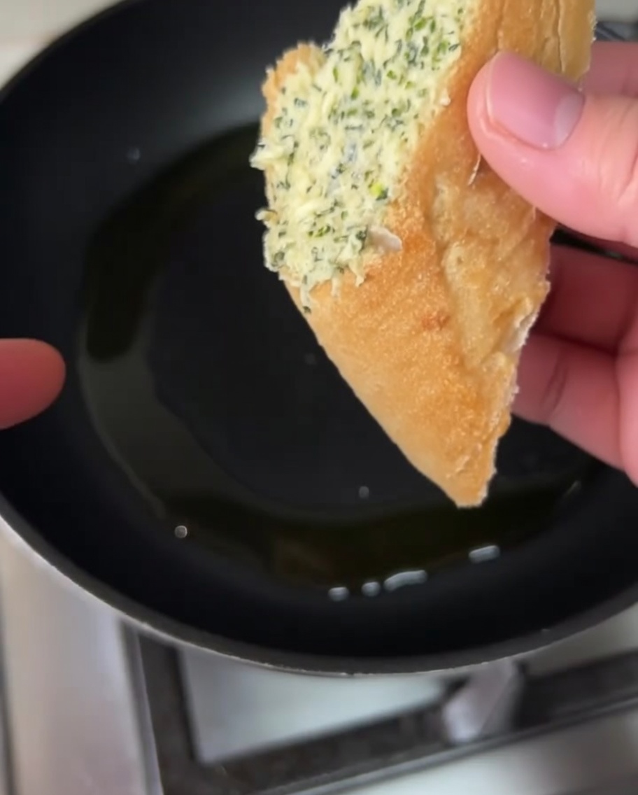 オリーブオイルを引いたフライパンで、ガーリックバターを塗った面を下にして焼いている様子。