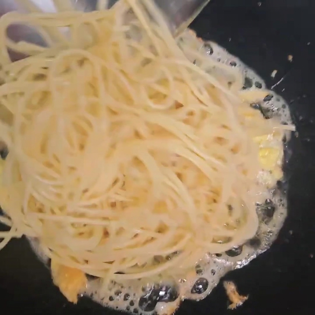 炒り卵の入ったフライパンに加えられる茹で上がったスパゲッティ。
