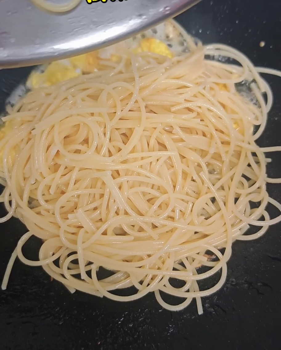 フライパンの中でスパゲッティと卵に加えられる茹でブロッコリーとミニトマト。