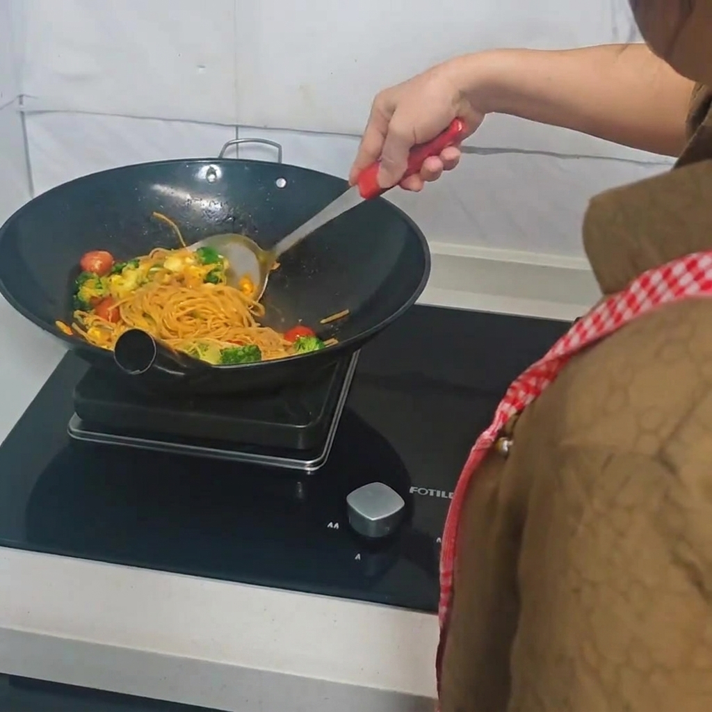 スパチュラを使ってフライパンで炒め合わせられているスパゲッティと具材。