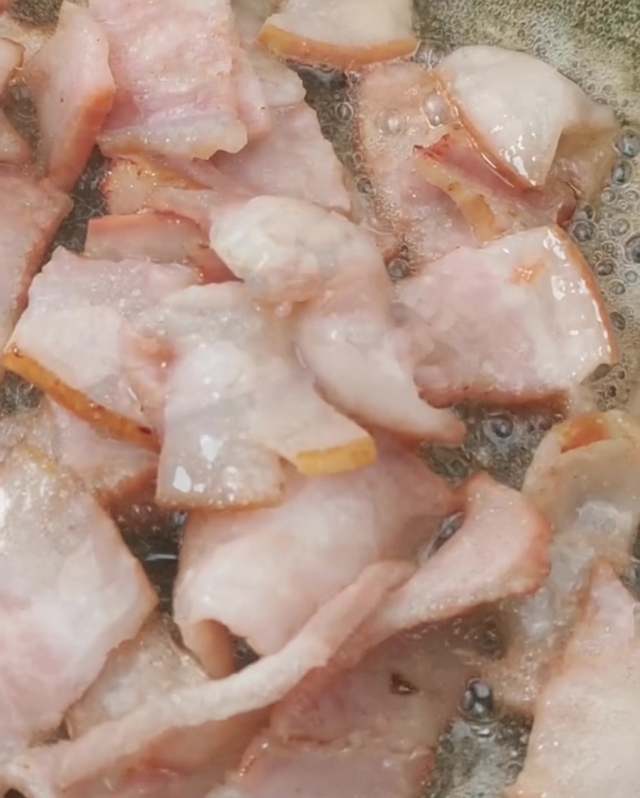 炒めたベーコンにトマトを加えている様子。