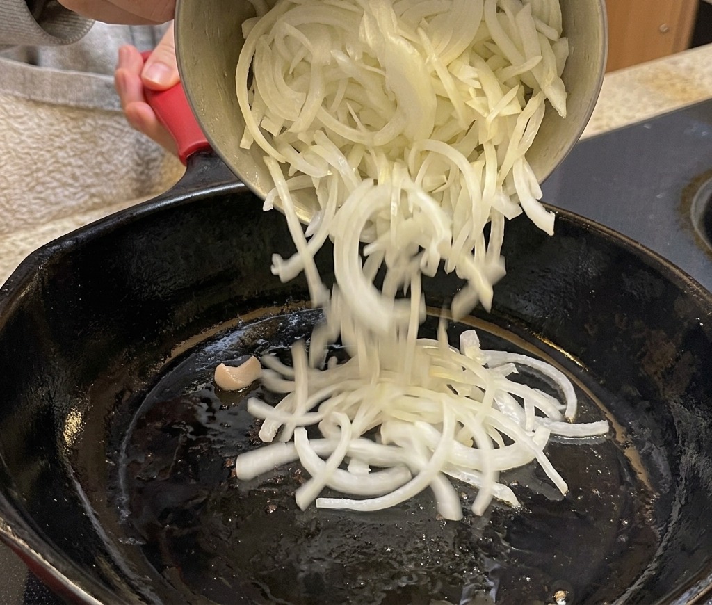 スライスした玉ねぎをフライパンに加えている様子。