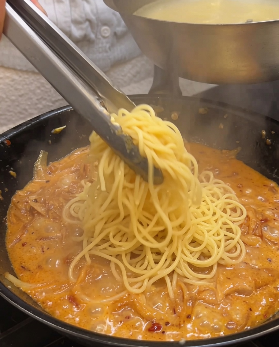 茹でたスパゲッティをフライパンに入れ、トングで混ぜ合わせている様子。