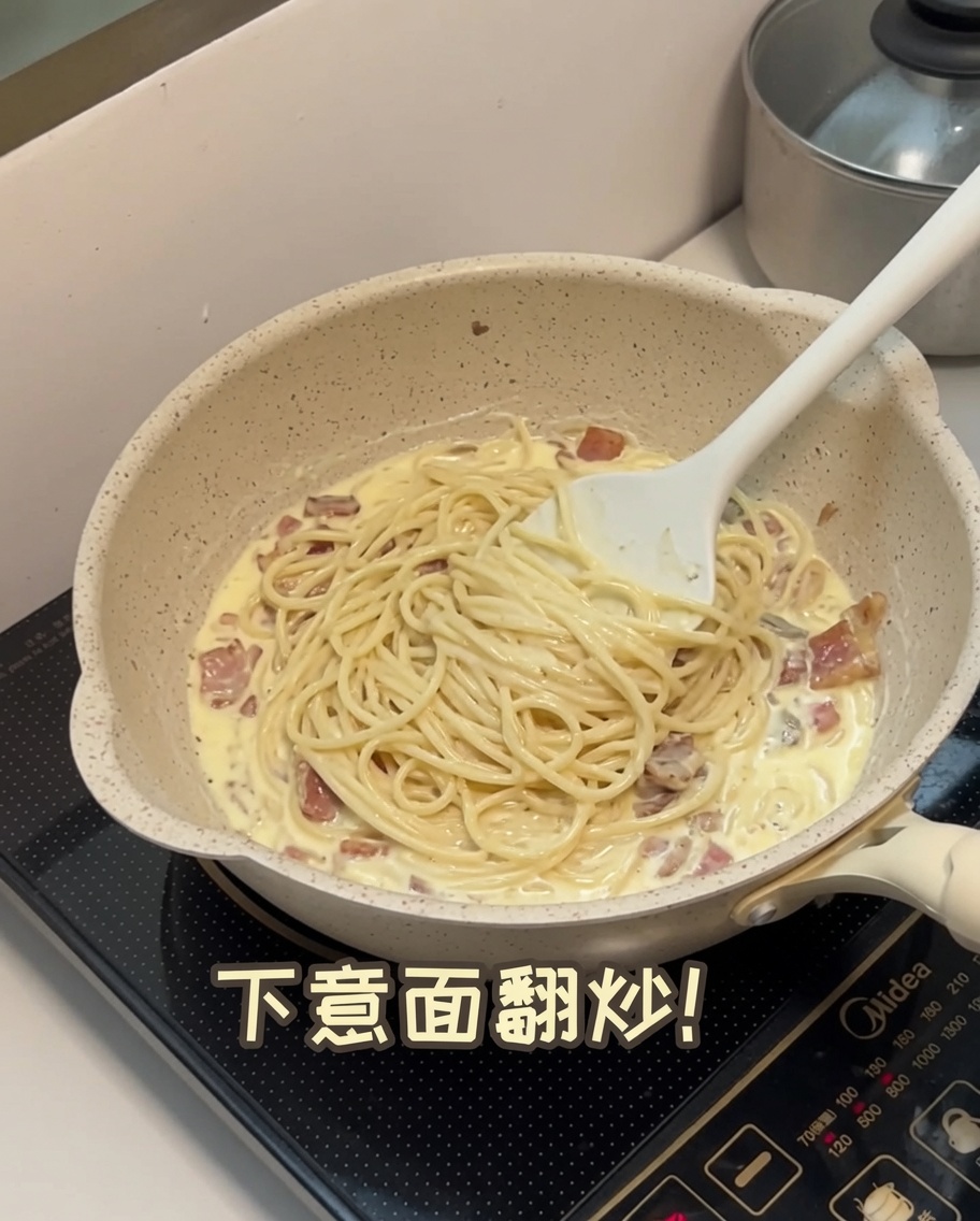 茹でたパスタをソースの入ったフライパンに加え、混ぜ合わせている様子