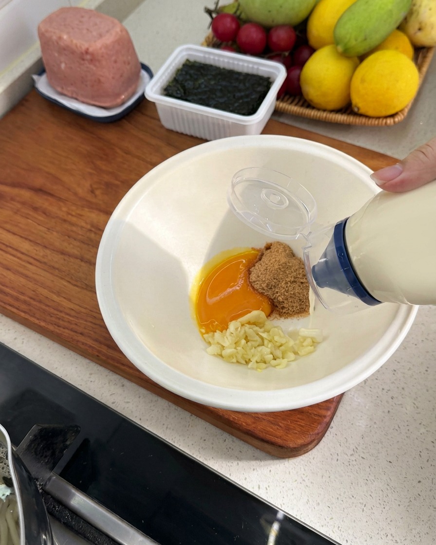 マヨネーズを他の材料が入ったどんぶりに絞り入れている様子。