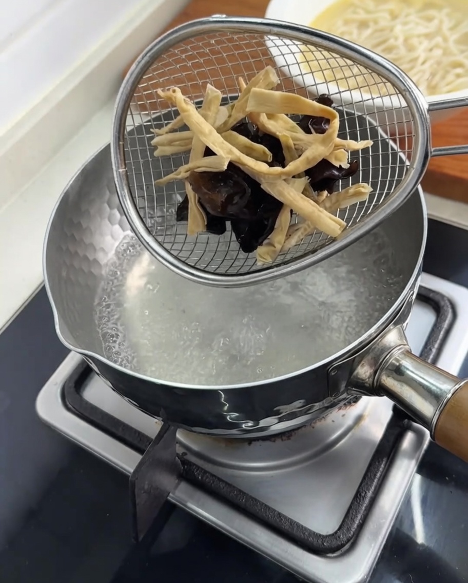 沸騰したお湯が入った鍋の中で、キクラゲとメンマをざるに入れて湯通ししている様子。