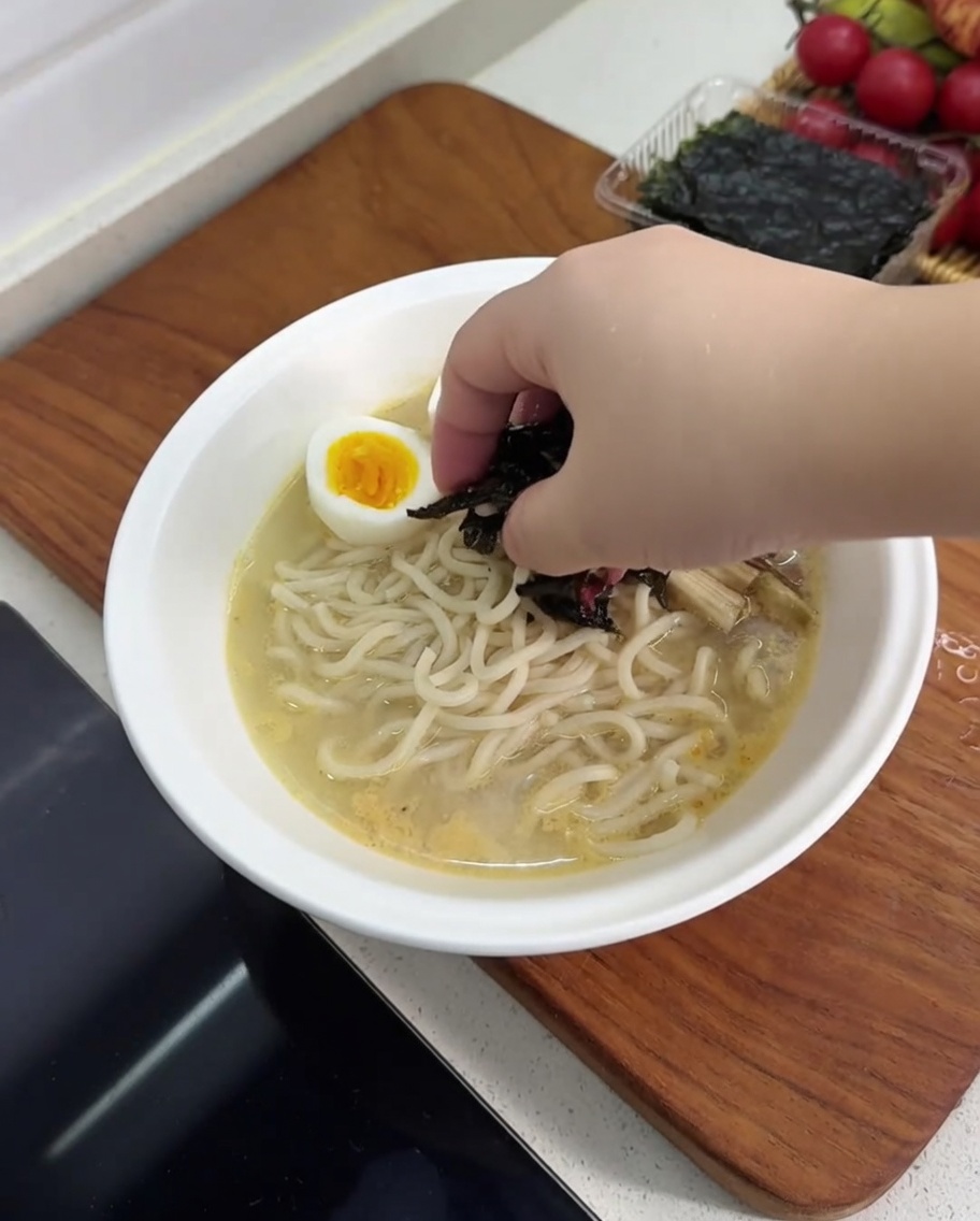 ラーメンに半分に切ったゆで卵、キクラゲ、メンマ、焼き海苔をトッピングしている様子。
