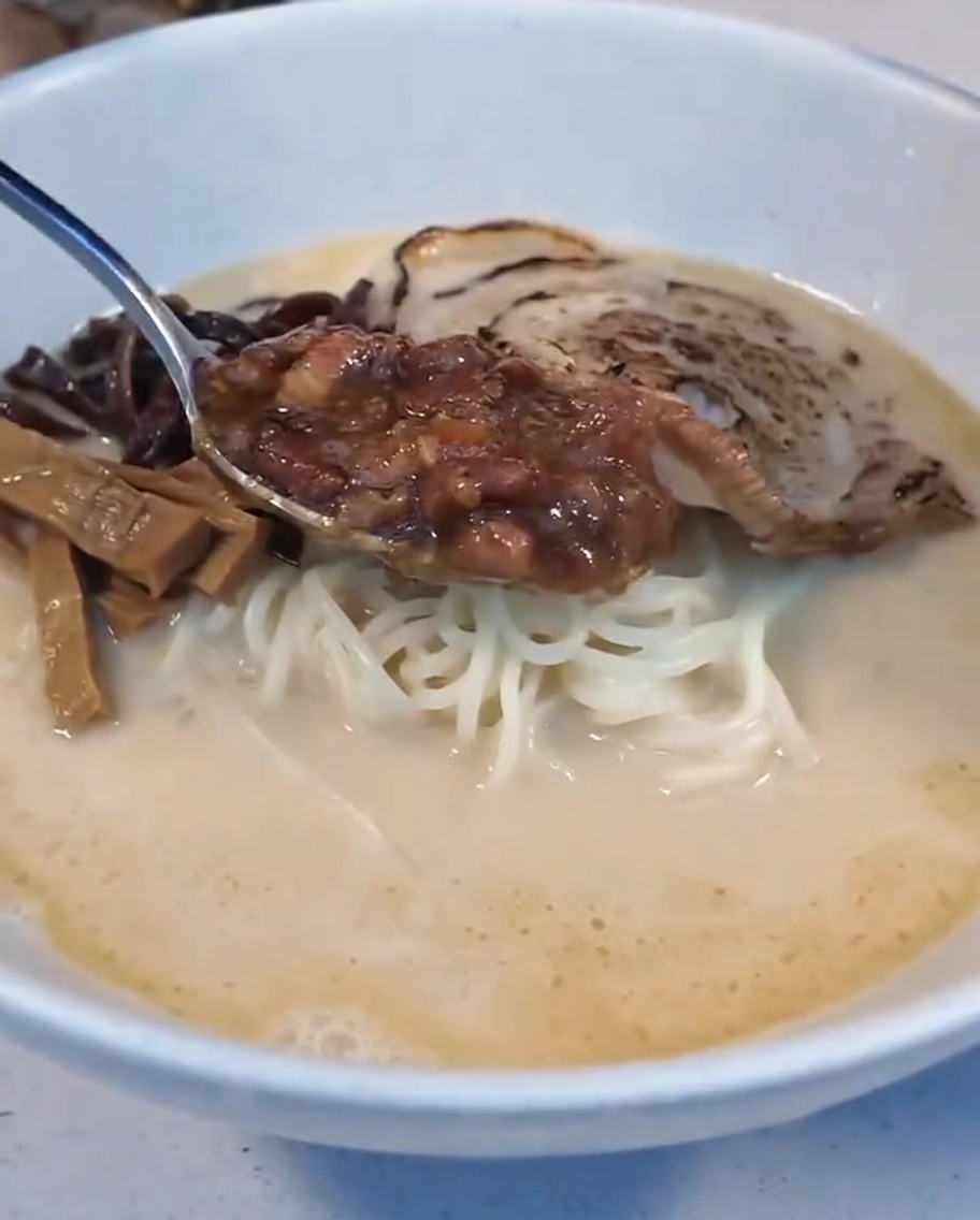 煮込み肉ダレと半熟卵をトッピングしている様子