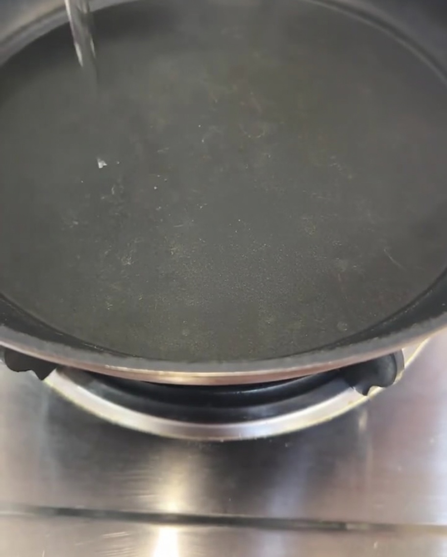 黒いフライパンの中央に調理油を細く注ぎ入れる様子。