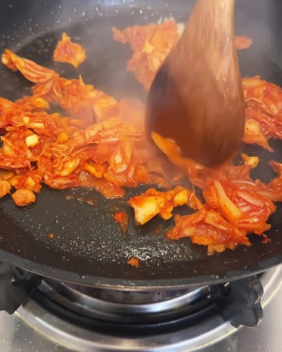炒めたキムチとにんにくが入ったフライパンに水を注いでいる様子。